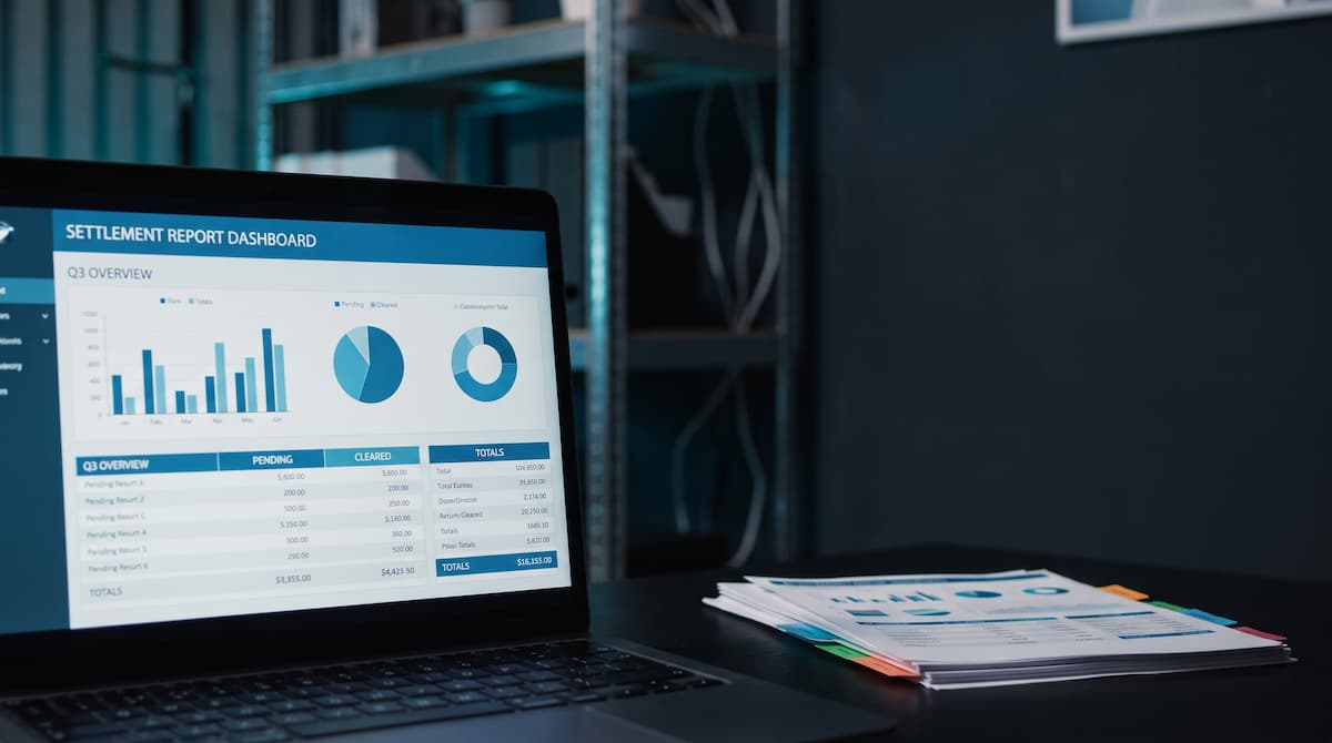 Settlement report dashboard on a laptop screen next to a stack of printed reports